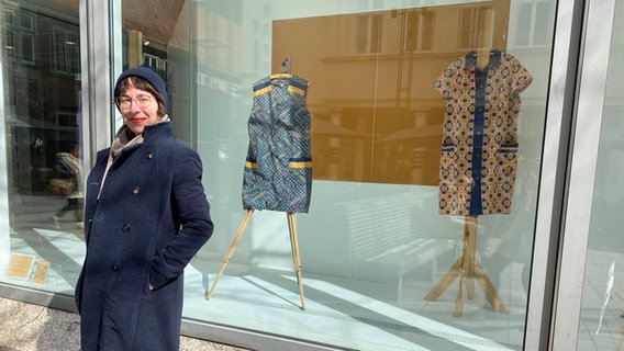 Ausstellungs-Kuratorin Stefanie Reis steht vor einem Schaufenster, in dem zwei Kittel zu sehen sind. © NDR.de Foto: Linda Ebener