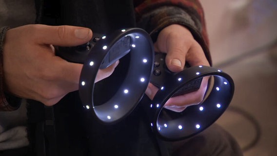 Zwei Hände halten leuchtende Controller einer VR-Brille © Screenshot NDR 