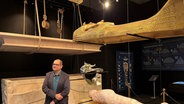 Ein Mann mit blauem Hemd, dunklem Sacko und Brille vor der Replik des Sarkophages von Tutanchamun - Ägyptologe Nacho Ares ist Kurator der Tutanchamun-Ausstellung in Hamburg © NDR Foto: Patricia Batlle