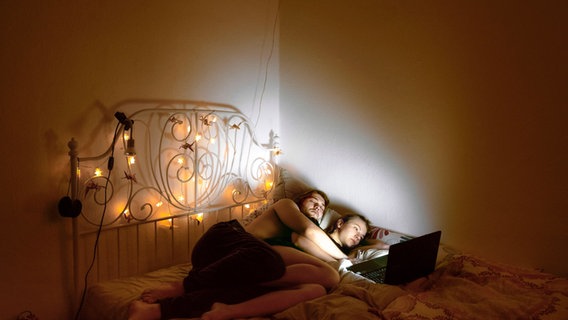 Ein junger Mann und eine junge Frau liegen in einem Bett und schauen auf einen hellen Laptop. © Valentin Goppel Foto: Valentin Goppel