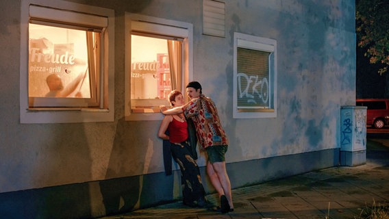 Eine junge Frau steht vor einem beleuchteten Fenster, vor ihr lehnt ein junger Mann. © Valentin Goppel Foto: Valentin Goppel