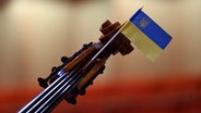 Eine Fahne der Ukraine steckt vor Beginn eines Konzerts an einem Saiten-Instrument des Kyiv Symphony Orchestras. © picture alliance/dpa | Robert Michael 
