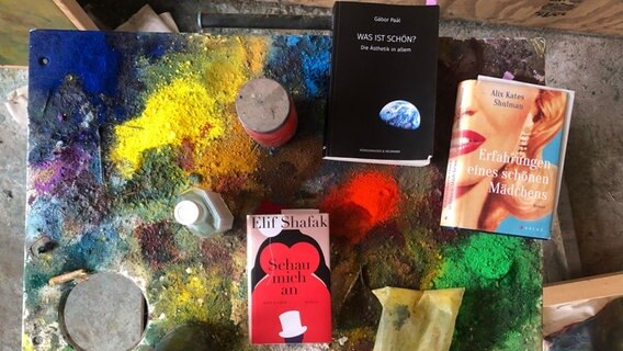 Die Bücher der Folge zum thema Schönheit liegen auf einem mit Farbe bespritztem Brett. © NDR 