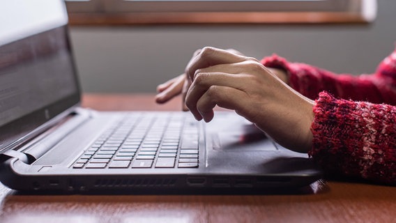 Seitenansicht einer weiblichen Hand, die auf einer Laptop-Tastatur in der Nähe des Fensters tippt © imago 