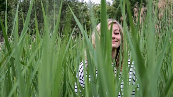 Ein Mädchen sitzt auf einer Wiese im hohen Gras uns schaut durch die Grashalme in die Kamera. © photocase Foto: bit.it