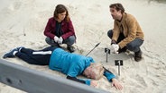 Ein Mann liegt tot im Sand - darüber knien eine Frau und ein Mann. © ZDF/Georges Pauly 