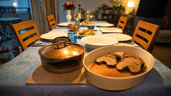 Eine Schüssel mit Fleisch und ein Topf stehen auf einem gedeckten Tisch. © NDR Foto: Tim Piotraschke