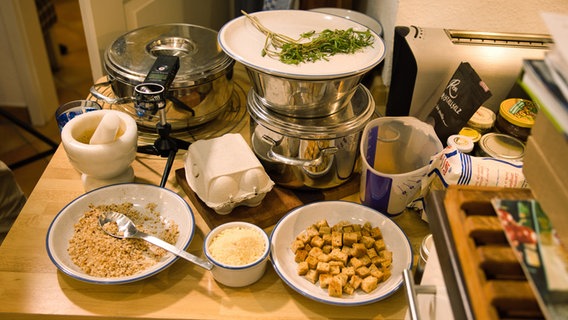 Croutons und Semmelbrösel aus frischem Roggen- und Emmer-Brot, Mayoran und Parmesan stehen auf einer Arbeitsplatte in einer Küche. © NDR Foto: Tim Piotraschke