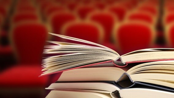 An open stack of books in front of the red rows of audience chairs.  © fotolia foto: auris, dondoc-foto