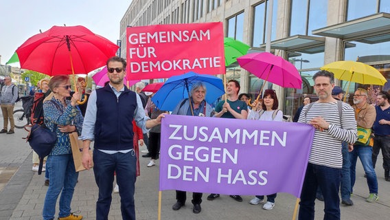 Eine Gruppe mit Plakaten und bunten Regenschirmen steht in einer Fußgängerzone. © NDR Foto: Svenja Estner