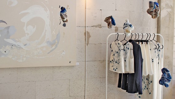 Auf dem Bild ist der Pop-Up-Store der Designerin Alina Klemm zu sehen. An der Wand hängt ein Gemälde, daneben ist ein Kleiderständer mit Mode aus ihrer eigenen Kollektion zu sehen. © NDR Foto: Alina Klemm
