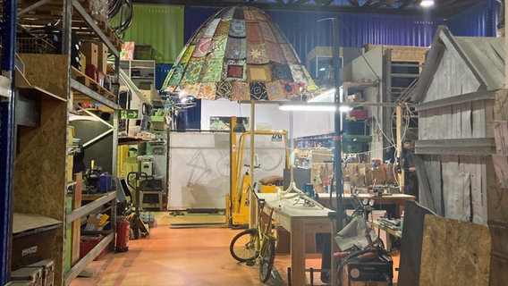 Blick auf eine Werkstatt mit einem bunten Schirm und einen gelben Fahrrad. © NDR Foto: Antonia Reiff