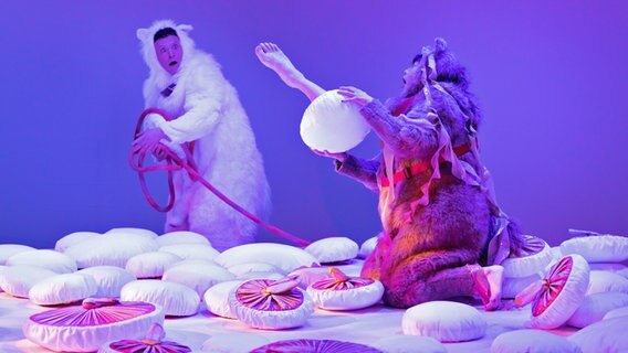 Zwei Darsteller in Hundekostümen spielen auf einer Bühne, die von Pilzen übersäht ist. © Hendrik Lietmann 