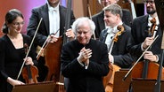 Ein Dirigent, András Schiff, steht mit dem Rücken zu einem Orchester und faltet voller Dankbarkeit die Händer vor der Brust. © picture alliance/CTK Photo/Michal Krumphanzl Foto: Michal Krumphanzl