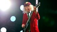 Ein älterer Mann mit roter Schuluniform und Mütze spielt Gitarre - Angus Young von AC/DC bei einem Auftritt 2024 in Hannover © IMAGO/Future Image 