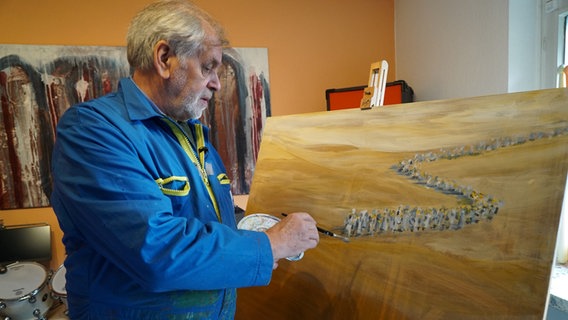 Ein Mann malt mit einem Pinsel auf einer Leinwand © NDR / Hauke Bülow Foto: Hauke Bülow