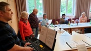 Mehrere Menschen sitzen und stehen um einen Tisch bei der Probe des Chors der Obdachlosen in Hannover © NDR Foto: Agnes Bührig