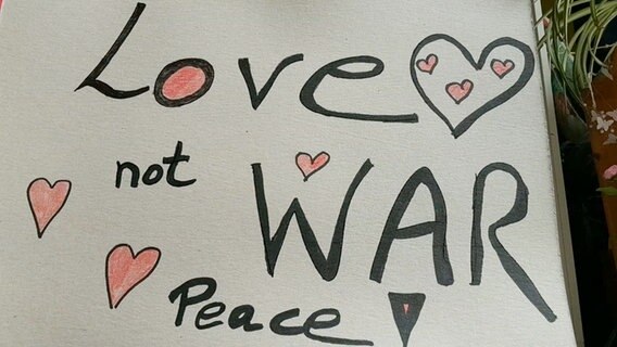 Ein selbstgemaltes Schild mit der Aufschrift "Love not war. Peace" und mehreren Herzen © NDR 