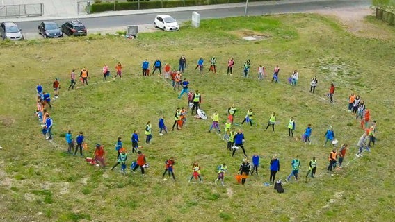 Etwa sechzig Menschen stehen in Form eines Peace-Zeichens auf einer Wiese © NDR 