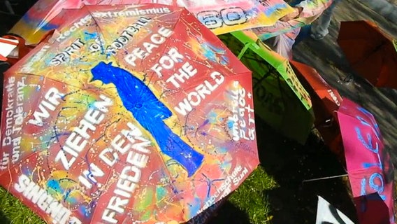 Mehrere beschriebene Regenschirme liegen auf dem Boden, auf einem steht unter anderem "Wir ziehen in den Frieden" und "Peace for the world" © NDR 