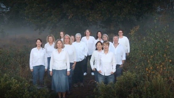Ein in weiß gekleideter Frauenchor mit fünfzehn Mitgliedern steht bei Nebel im Wald © NDR 