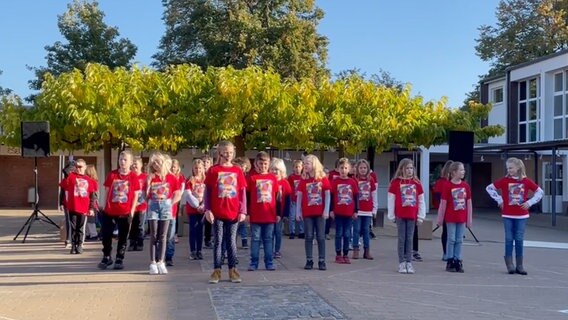 Etwa zwanzig Grundschulkinder in roten T-Shirts stehen in Reihen auf dem Schulhof © NDR 