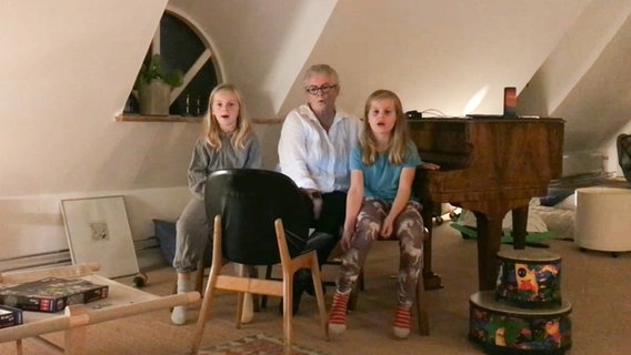 Eine Frau und zwei blonde Mädchen sitzen vor einem braunen Flügel und singen © NDR 