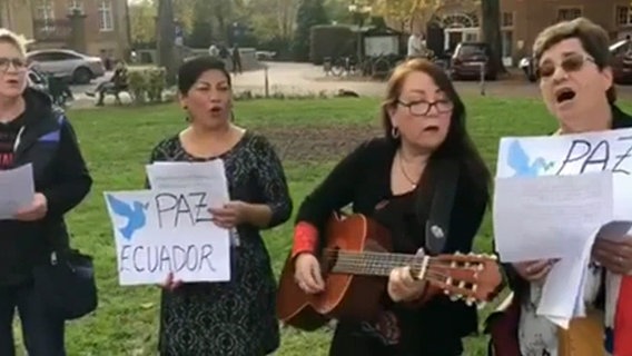 Vier Frauen stehen singend auf einer Wiese und halten Blätter mit den Worten "Paz" und "Ecuador", eine spielt Gitarre © NDR 