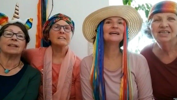 Vier Frauen mit verschiedenen Accessoires in Regenbogenfarben singen und schauen in die Kamera © NDR 