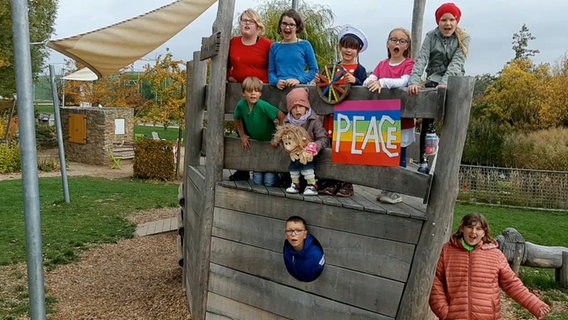 Neun Kinder stehen mit einem Plakat mit der Aufschrift "Peace" auf einem Klettergerüst © NDR 