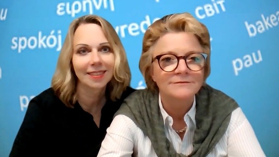 Zwei blonde Frauen sitzen vor einem virtuellen Hintergrund, auf dem in verschiedenen Sprachen das Wort "Frieden" steht © NDR 