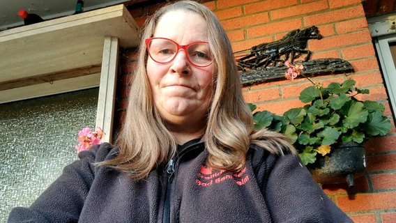 Eine Frau mit dunkelblonden Haaren und roter Brille steht vor einer Hauswand © NDR 