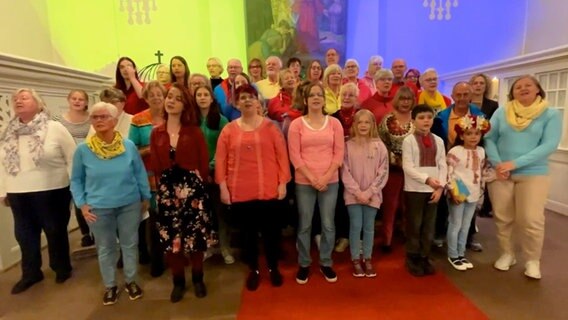 Etwa dreißig Erwachsene und ein paar Kinder stehen in einer blau und gelb beleuchteten Kirche und singen © NDR 