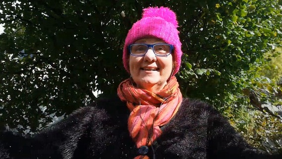 Eine Frau mit Brille und pinker Pudelmütze steht vor einem Baum © NDR 