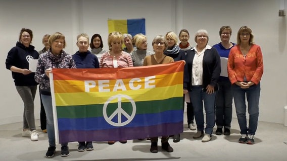 Vierzehn Frauen stehen zusammen und halten eine Regenbogenfahne mit der Aufschrift "Peace". Hinter ihnen hängt eine Ukraine-Flagge © NDR 