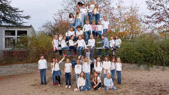 Knapp vierzig Kinder in weißen Shirts und Jeans haben sich in vier Etagen vor und auf einem Klettergerüst drapiert und schauen in die Kamera. © NDR 