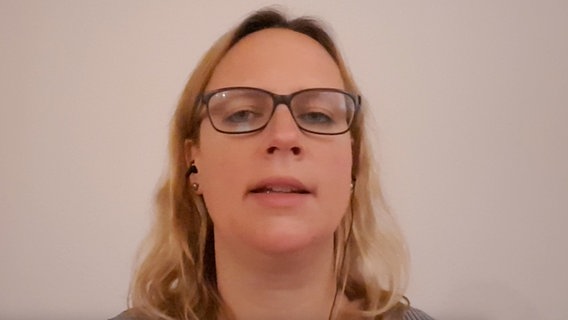 Eine blonde Frau mit schwarzer Brille und In-Ear-Kopfhörern blickt in die Kamera. © NDR 