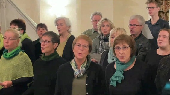 Fünfzehn grün gekleidete Menschen stehen in mehreren Reihen in einer Kirche und singen © NDR 