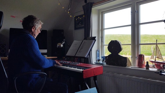 Ein Mann sitzt vor einem Fenster an seinem roten E-Piano © NDR Foto: Peer-Axel Kroeske