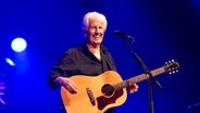 Graham Nash steht mit einer Gitarre auf der Bühne und lacht. © IMAGO / agefotostock 
