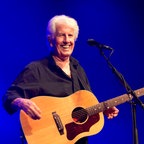 Graham Nash steht mit einer Gitarre auf der Bühne und lacht. © IMAGO / agefotostock 