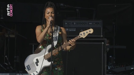 Eine Frau mit Rastalocken spielt auf einer Bühne E-Bass und singt in ein Mikrofon. © NDR 