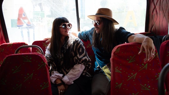 Zwei Menschen mit Sonnenbrillen sitzen in einem Bus. © GUMO Foto: GUMO