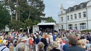 Menschen stehen vor einer Bühne neben dem Maritim Hotel am Timmendorfer Strand © NDR Foto: Doreen Pelz