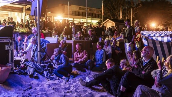 Menschen sitzen am Strand und schauen auf eine Bühne © Felix König Foto: Felix König