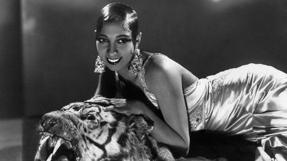 Josephine Baker lehnt auf einem Tigerkopf und lächelt in die Kamera. © HIP | Keystone Archives Foto: William Gottlieb