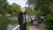 Ein lachender Mann lehnt an der Brüstung eines Zauns vor einem Teich in einem Park. © Michael Laages Foto: Michael Laages