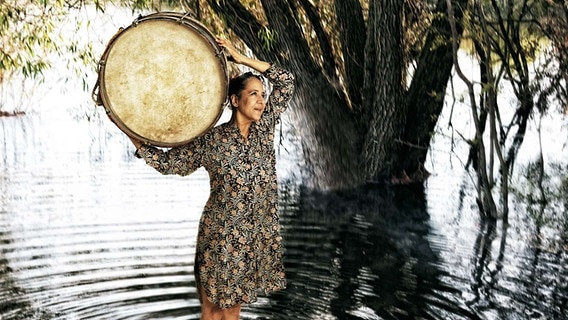 Eine im Wasser stehende Frau hält eine Trommel. © Per Morten Abrahmasen Foto: Per Morten Abrahmasen