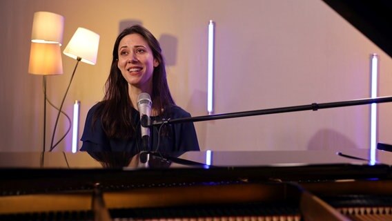Eine Sängering mit langen dunklen Haaren sitzt lächelnd mit geschlossenen Augen an einem Mikrofon. © NDR Foto: Franziska Dieckmann