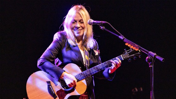 Eine lachende Frau steht vor einem Mikrofon und spielt Akustikgitarre. © picture alliance / NurPhoto | Mairo Cinquetti Foto: Mairo Cinquetti